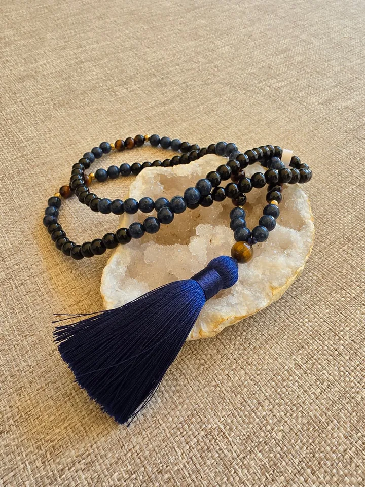 Le mala posé sur une géode, perles d'onyx noir et sodalite ponctuées d'œil de tigre, terminé par un pompon bleu nuit
