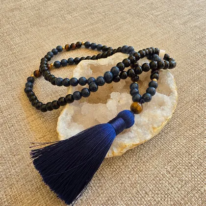 Le mala posé sur une géode, perles d'onyx noir et sodalite ponctuées d'œil de tigre, terminé par un pompon bleu nuit