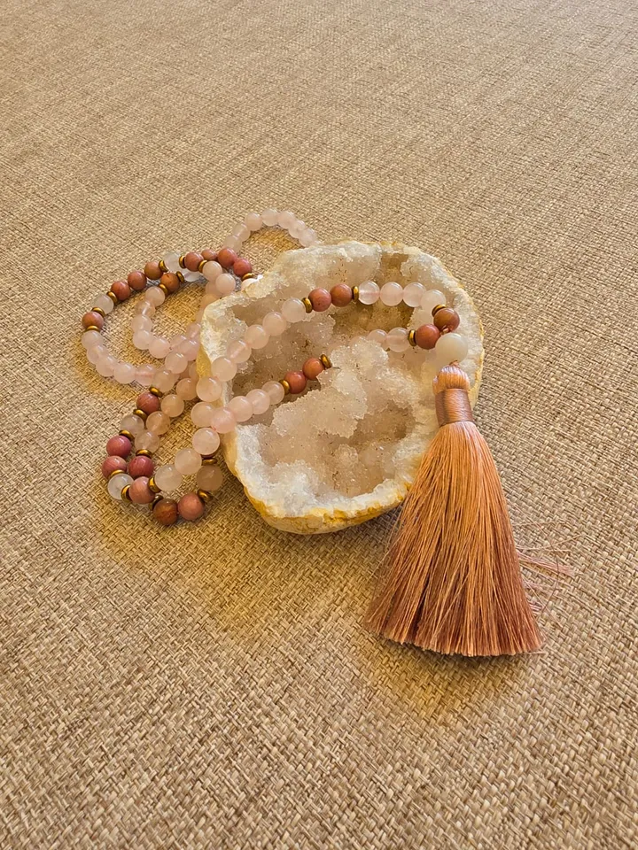 Le mala posé sur une géode, perles de quartz rose translucide alternées de perles de rhodonite, terminé par un pompon rose cuivré