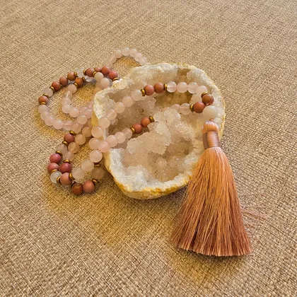 Le mala posé sur une géode, perles de quartz rose translucide alternées de perles de rhodonite, terminé par un pompon rose cuivré