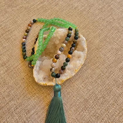 Le mala posé sur une géode, perles d'aventurine verte translucide et d'agate indienne, terminé par un pompon vert profond