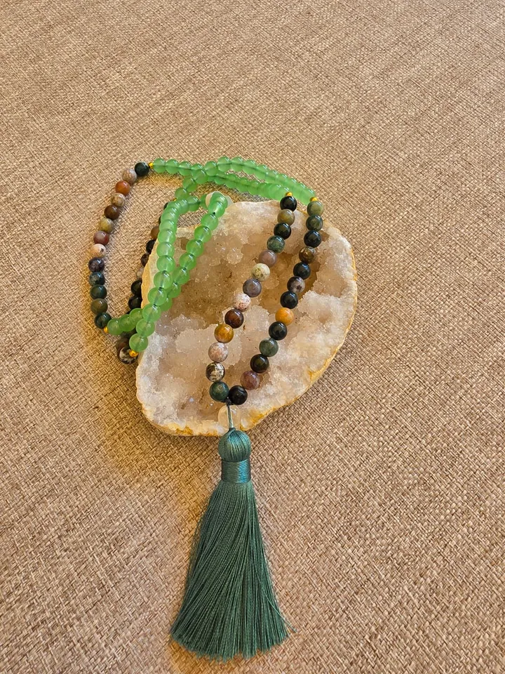 Le mala posé sur une géode, perles d'aventurine verte translucide et d'agate indienne, terminé par un pompon vert profond