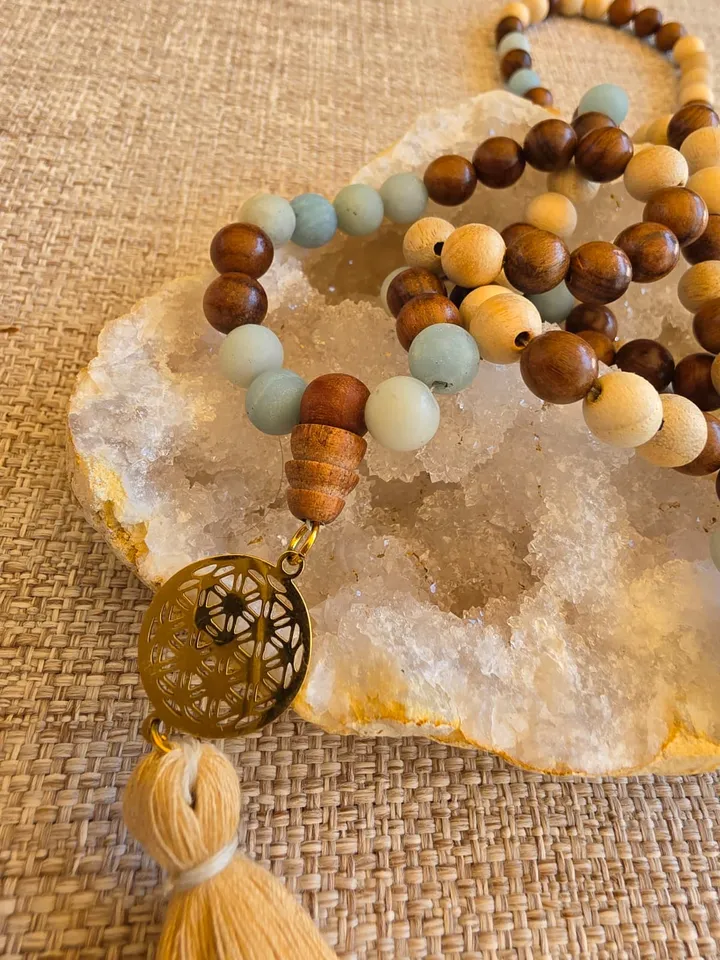 Gros plan sur les perles de bois bicolore et d'amazonite dépoli, la breloque fleur de vie et le pompon beige.