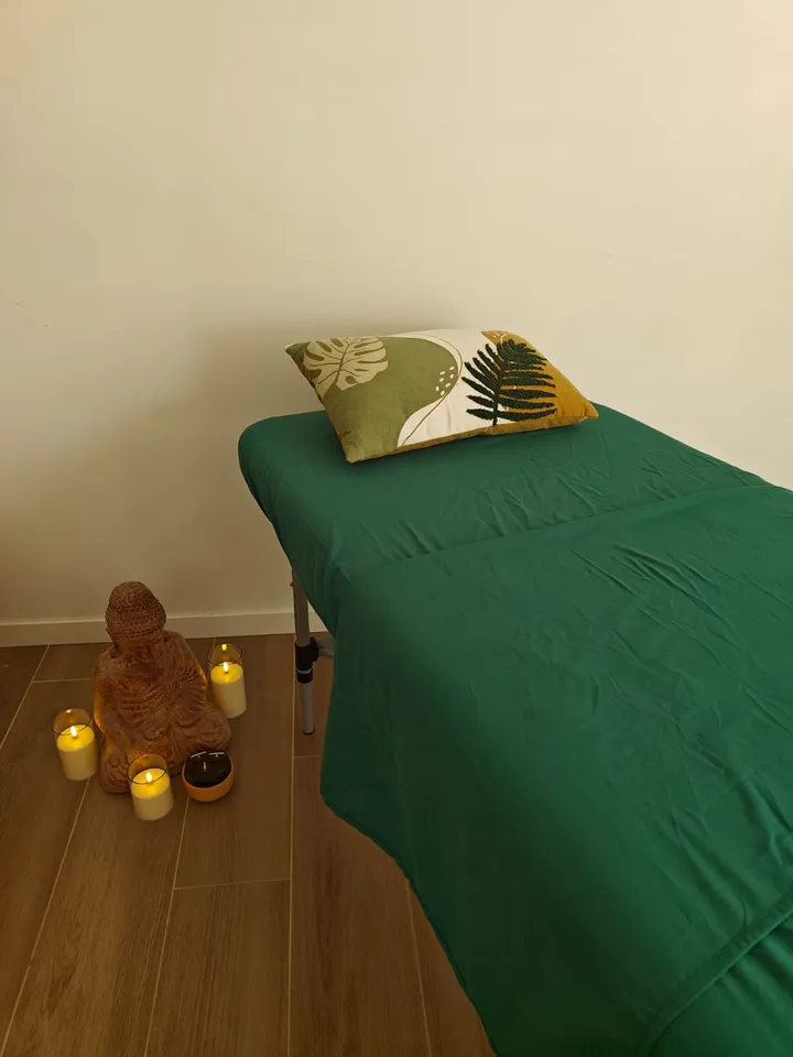 La table de soin du cabinet, drapée de vert, un coussin brodé de feuillages posé à la tête ; au sol, une statuette de Bouddha en terre cuite entourée de bougies allumées