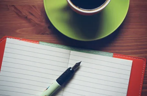 Carnet ouvert, stylo plume et tasse verte sur une table en bois